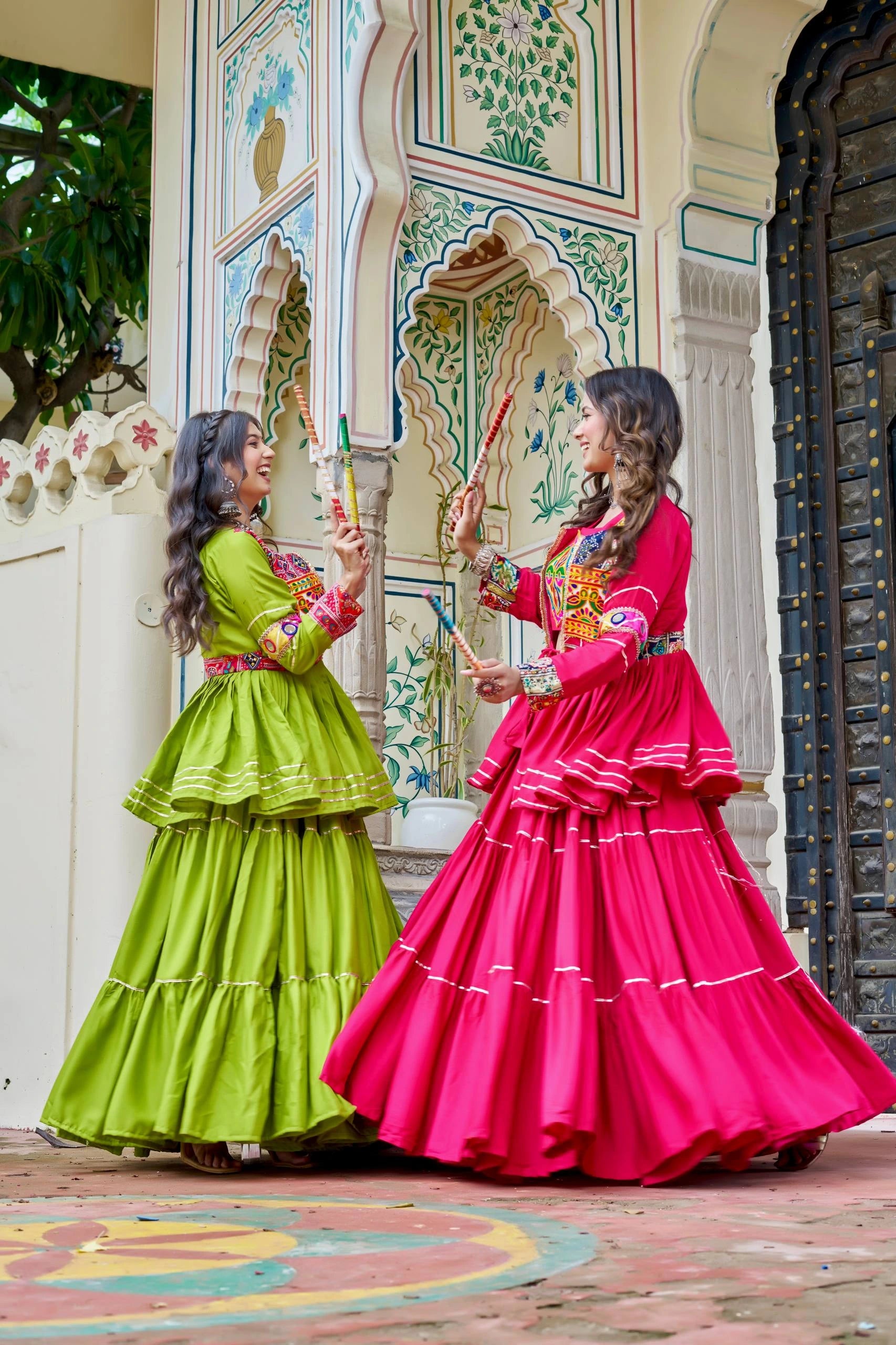 Two women in colorful traditional dresses standing in front of a decorated wall.
